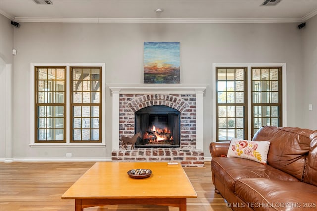 living room with light wood-style flooring, visible vents, baseboards, a brick fireplace, and crown molding