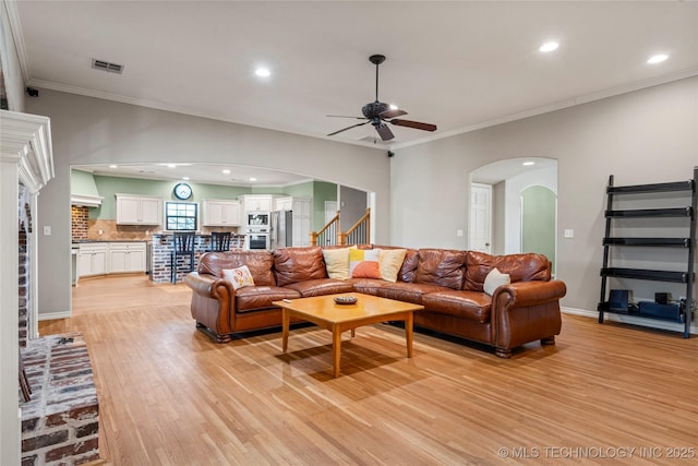 living area featuring arched walkways, visible vents, ornamental molding, stairway, and light wood-type flooring