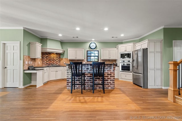 kitchen with a breakfast bar area, stainless steel appliances, premium range hood, light wood finished floors, and dark countertops