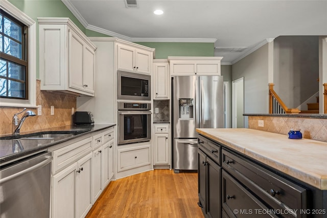 kitchen featuring stainless steel appliances, light wood finished floors, a sink, and crown molding