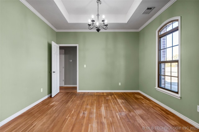 empty room featuring a raised ceiling, visible vents, an inviting chandelier, wood finished floors, and baseboards