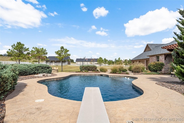 outdoor pool featuring a diving board, a patio area, and fence