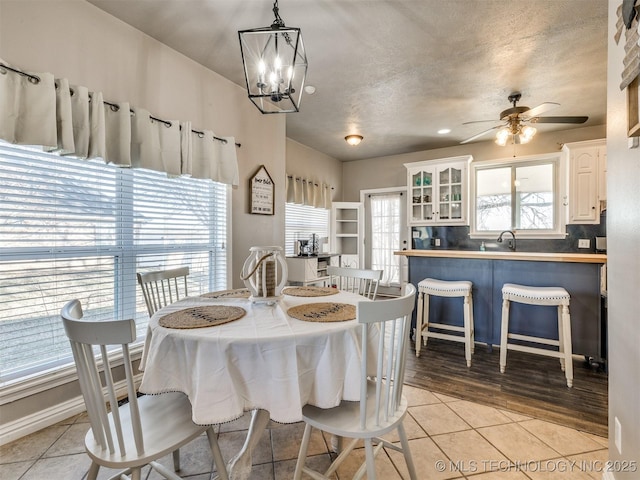 dining space featuring ceiling fan with notable chandelier, a textured ceiling, and light tile patterned flooring