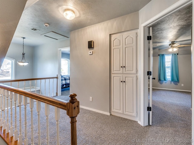 hallway featuring carpet, visible vents, a textured ceiling, and baseboards