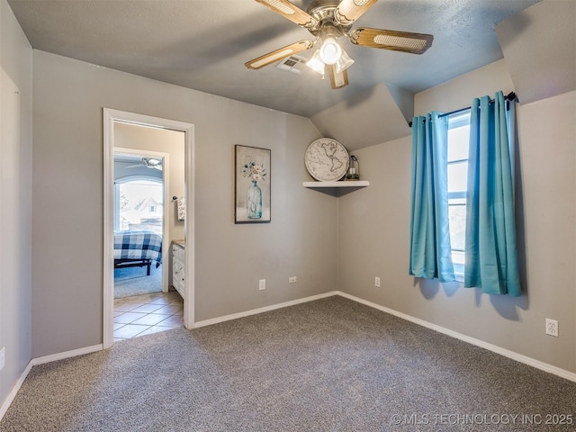 empty room featuring carpet floors, visible vents, vaulted ceiling, and a ceiling fan