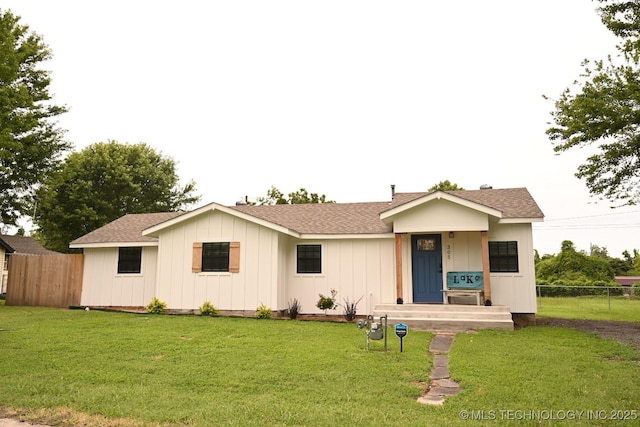 ranch-style home with a shingled roof, fence, a front lawn, and board and batten siding