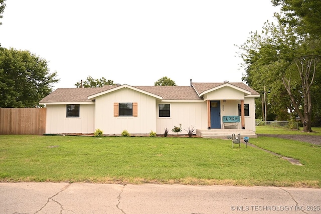 ranch-style home featuring a shingled roof, a front yard, and fence