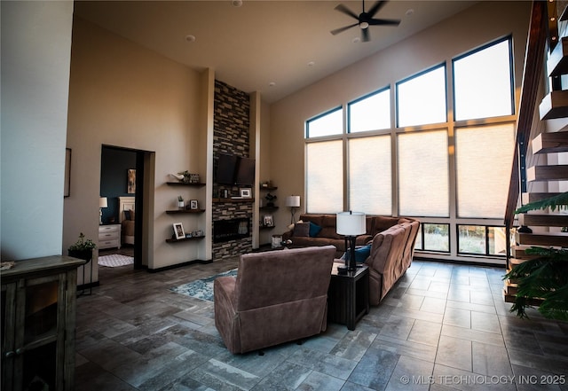 living room featuring a towering ceiling, a ceiling fan, and a stone fireplace