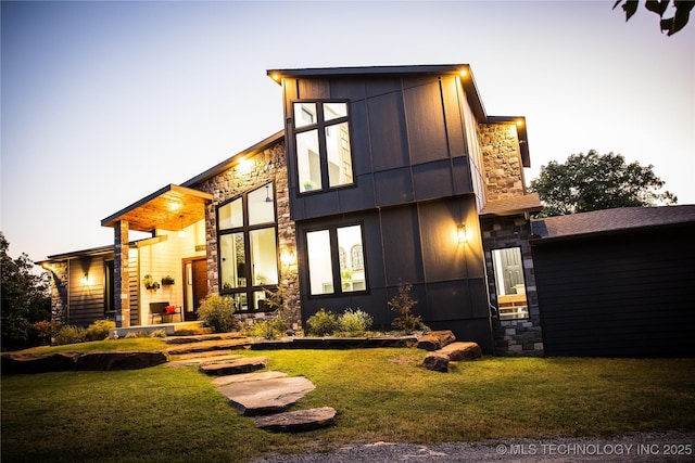 back of property featuring stone siding and a yard