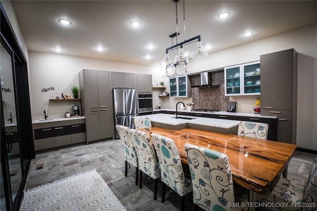 kitchen with open shelves, tasteful backsplash, light countertops, appliances with stainless steel finishes, and wall chimney exhaust hood