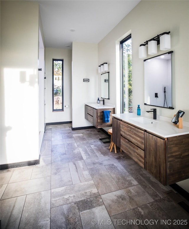 full bathroom with two vanities, a sink, and baseboards