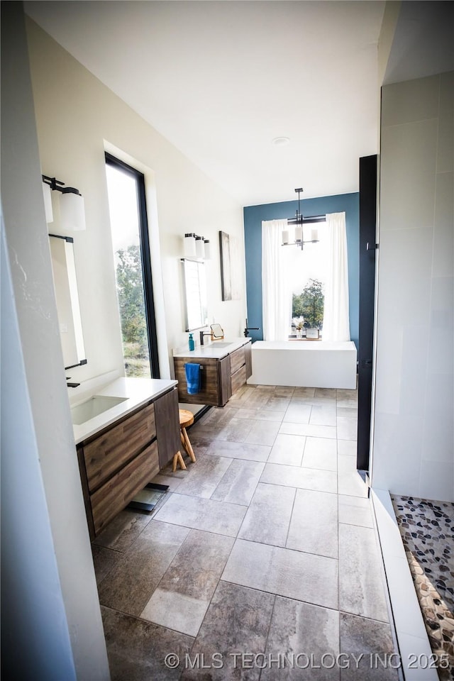 bathroom featuring a wealth of natural light, two vanities, a sink, and an inviting chandelier