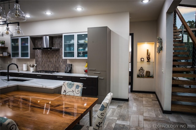 kitchen featuring wall chimney exhaust hood, stone finish flooring, stainless steel gas cooktop, a sink, and recessed lighting