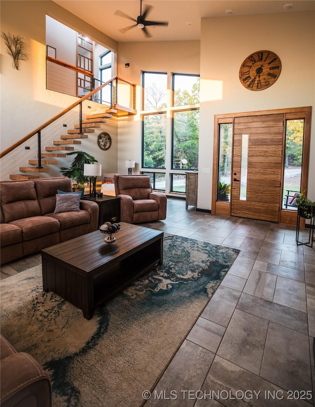 living room with a ceiling fan, stairway, a towering ceiling, and a healthy amount of sunlight