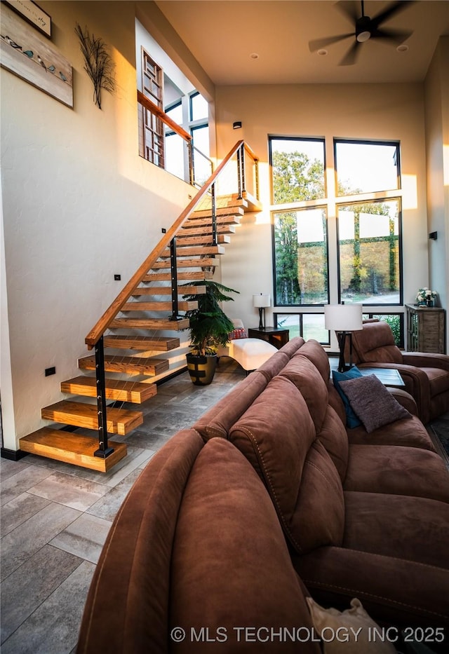 living area with ceiling fan, a high ceiling, stairway, and stone tile floors