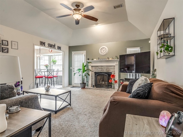 carpeted living room with vaulted ceiling, a brick fireplace, visible vents, and a ceiling fan