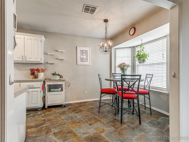 dining area with visible vents, stone finish floor, a textured ceiling, a chandelier, and baseboards