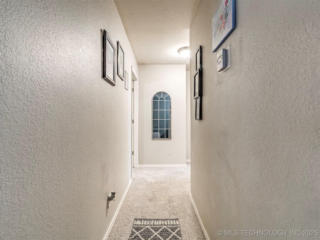 corridor with carpet floors, baseboards, a textured ceiling, and a textured wall