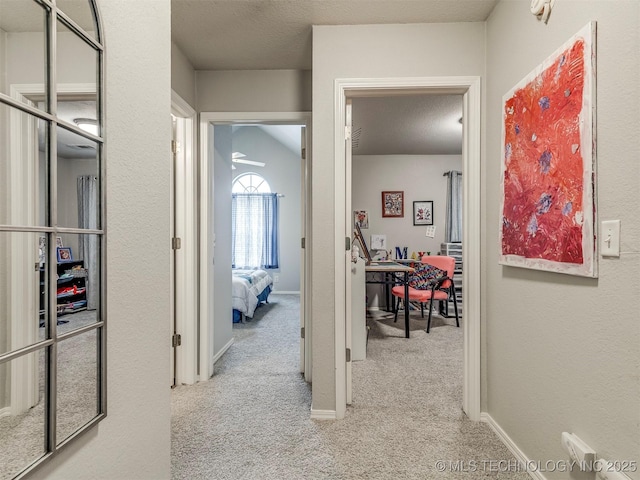 hall featuring a textured ceiling, carpet flooring, and baseboards