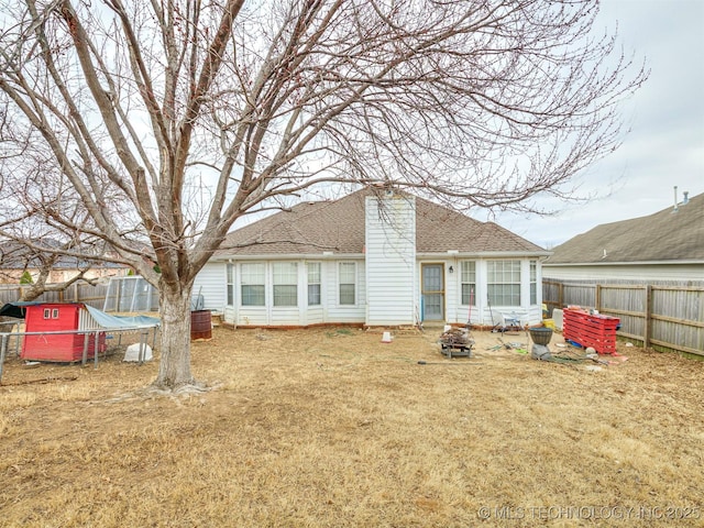 back of house with a fenced backyard, a chimney, a fire pit, and a shingled roof