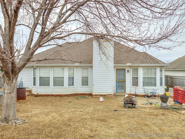 rear view of property featuring an outdoor fire pit, a shingled roof, a lawn, a chimney, and fence