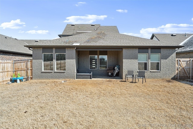 back of house featuring brick siding, a fenced backyard, and roof with shingles