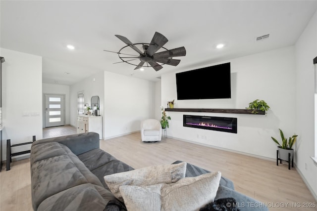 living area with recessed lighting, visible vents, a glass covered fireplace, ceiling fan, and wood finished floors