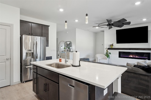 kitchen featuring dark brown cabinetry, stainless steel appliances, a sink, open floor plan, and decorative light fixtures