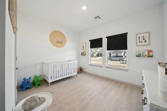 bedroom featuring a crib, wood finished floors, visible vents, and recessed lighting