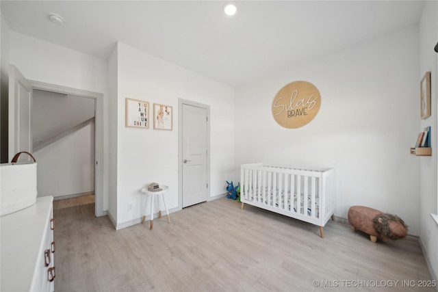 bedroom featuring baseboards, a crib, and light wood-style floors