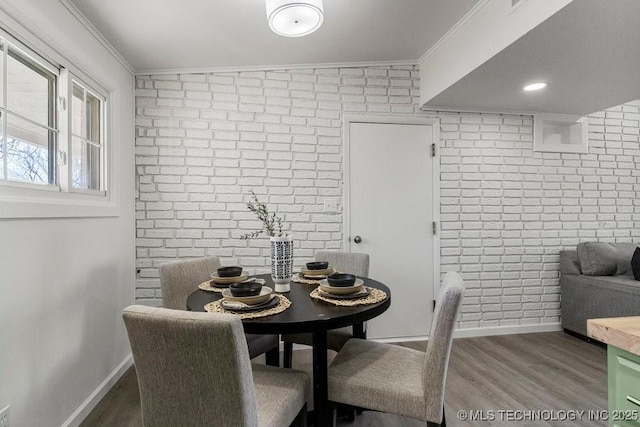 dining room featuring brick wall, wood finished floors, baseboards, and ornamental molding