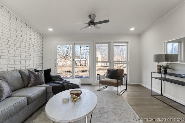 living room with brick wall, crown molding, baseboards, recessed lighting, and wood finished floors