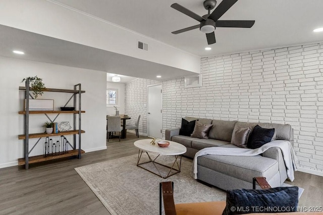 living area featuring wood finished floors, visible vents, brick wall, ceiling fan, and crown molding