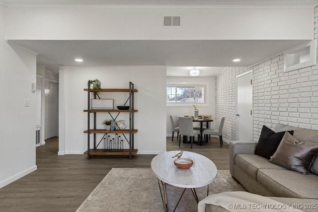 living room featuring visible vents, brick wall, baseboards, and wood finished floors