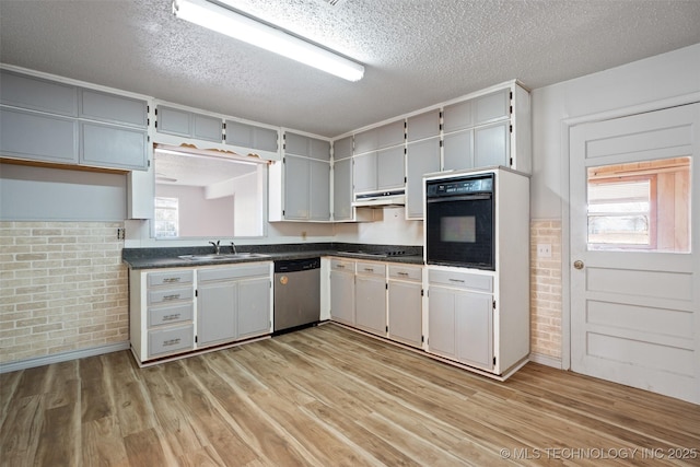 kitchen featuring dark countertops, light wood-style flooring, a sink, a textured ceiling, and black appliances