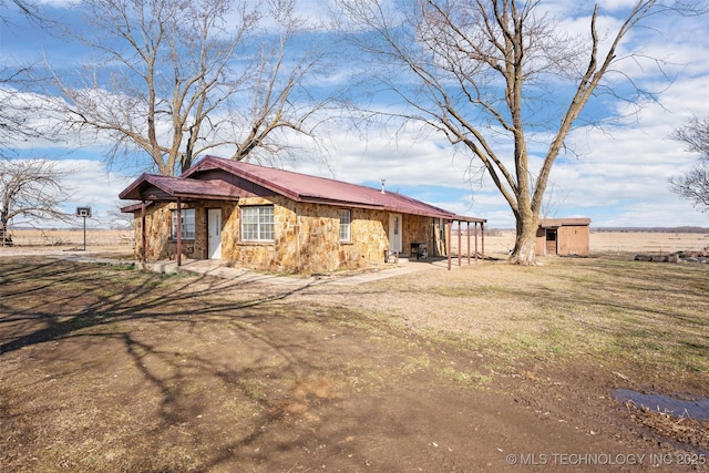 exterior space featuring an outbuilding, stone siding, a storage shed, and dirt driveway