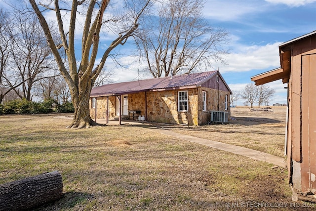 exterior space with stone siding, central AC unit, metal roof, and a front yard