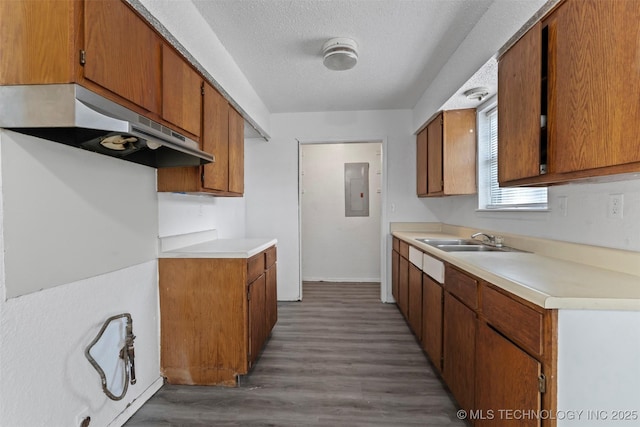 kitchen with electric panel, brown cabinets, light countertops, a textured ceiling, and under cabinet range hood