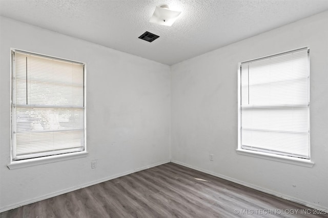 unfurnished room featuring visible vents, a textured ceiling, baseboards, and wood finished floors