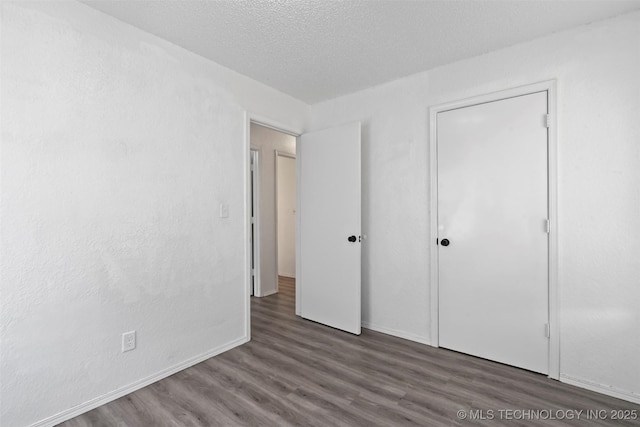 unfurnished bedroom with a textured ceiling, baseboards, and wood finished floors