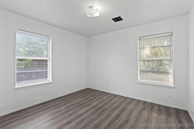 empty room featuring visible vents, a textured ceiling, baseboards, and wood finished floors