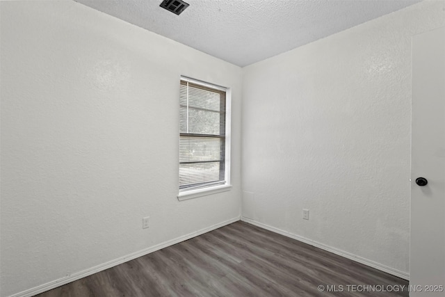 empty room with a textured ceiling, dark wood-style flooring, visible vents, and baseboards