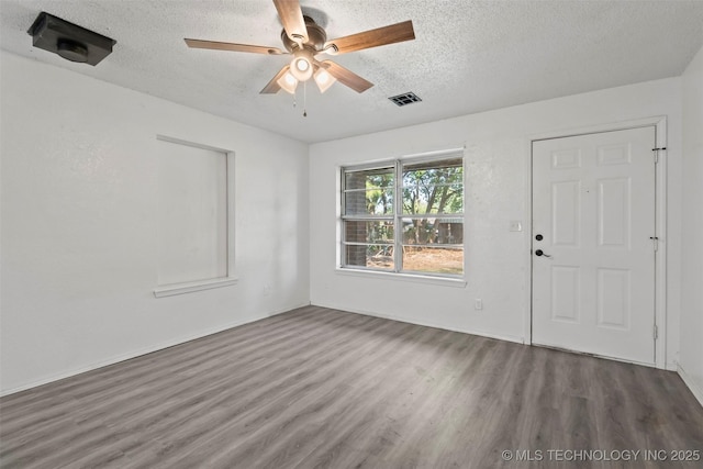 empty room featuring a textured ceiling, visible vents, wood finished floors, and a ceiling fan