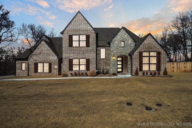 view of front facade with brick siding, a shingled roof, fence, stone siding, and a front yard