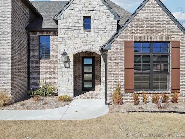 doorway to property with stone siding, brick siding, and roof with shingles