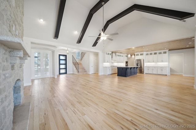 unfurnished living room featuring a ceiling fan, high vaulted ceiling, light wood-type flooring, beamed ceiling, and stairs