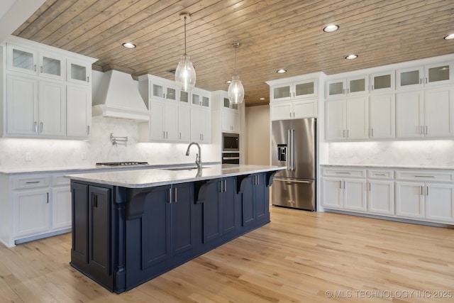 kitchen featuring wooden ceiling, light wood-style flooring, appliances with stainless steel finishes, premium range hood, and a sink