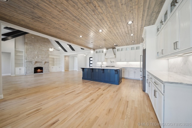 kitchen with lofted ceiling with beams, freestanding refrigerator, custom exhaust hood, a kitchen bar, and white cabinetry