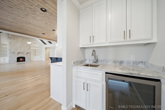 bar with wine cooler, built in shelves, a large fireplace, a sink, and a ceiling fan