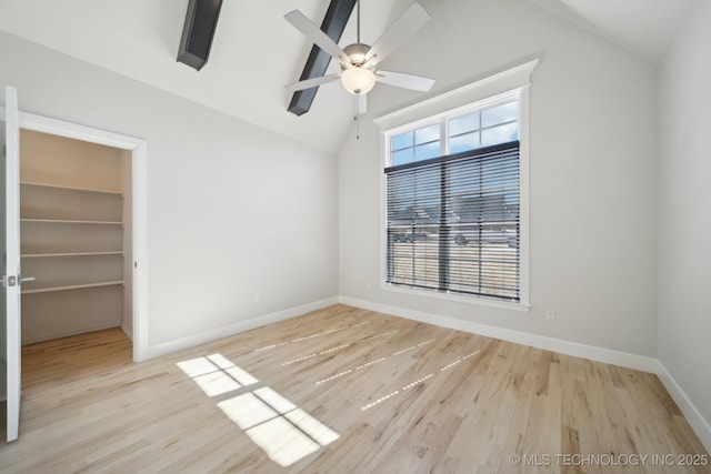 unfurnished bedroom featuring lofted ceiling, a walk in closet, baseboards, and wood finished floors